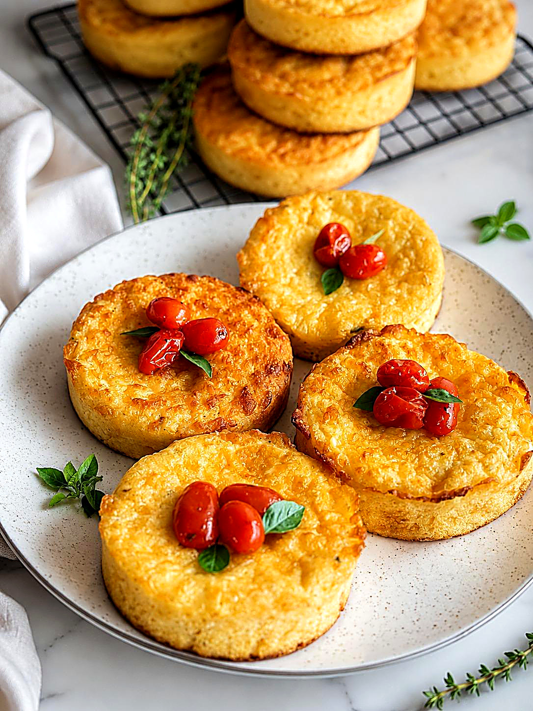 Quatro tortinhas douradas em prato de cerâmica, com tomate cereja e manjericão